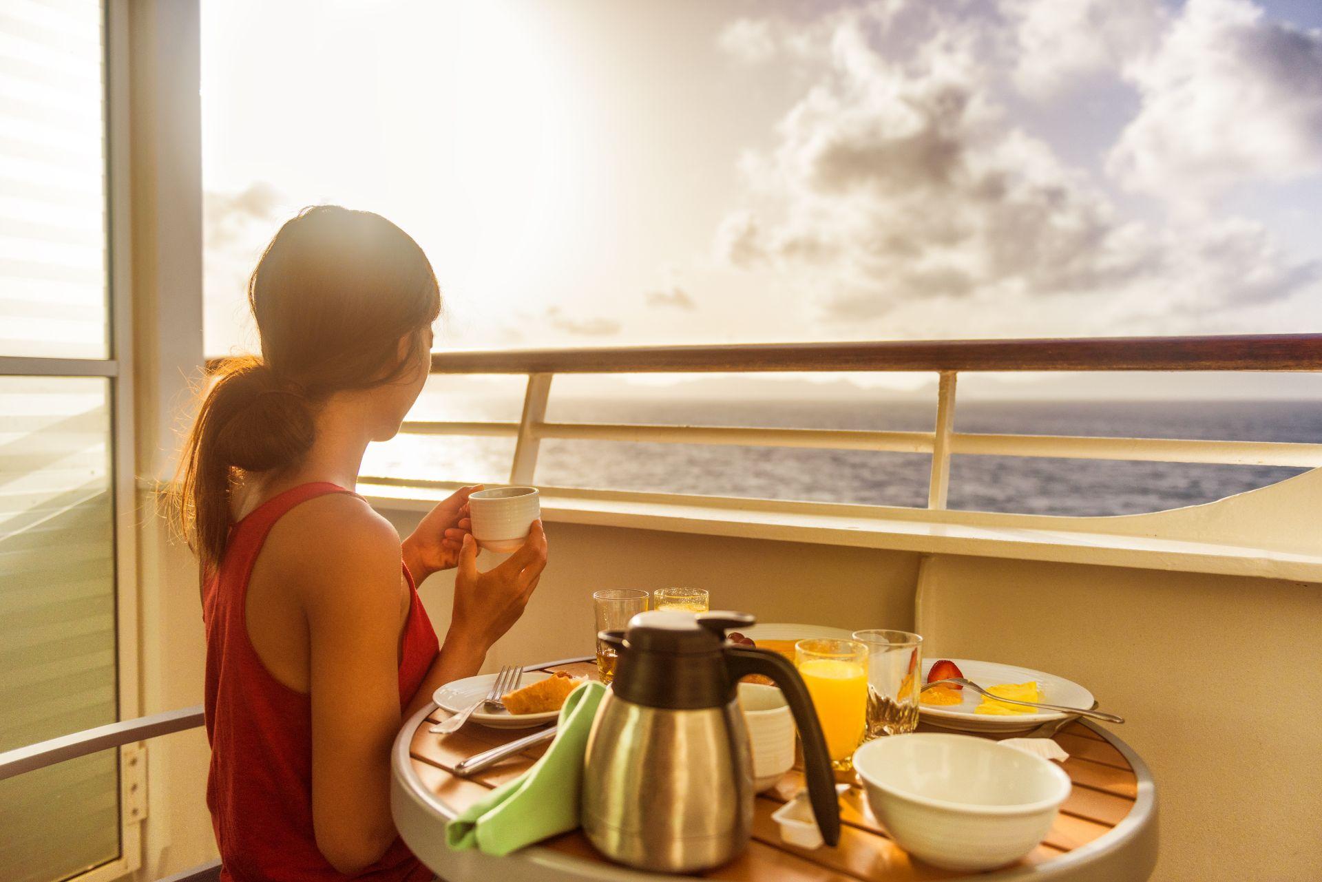 Cruise ship woman eating breakfast from room service on suite balcony enjoying morning view of Caribbean ocean.
