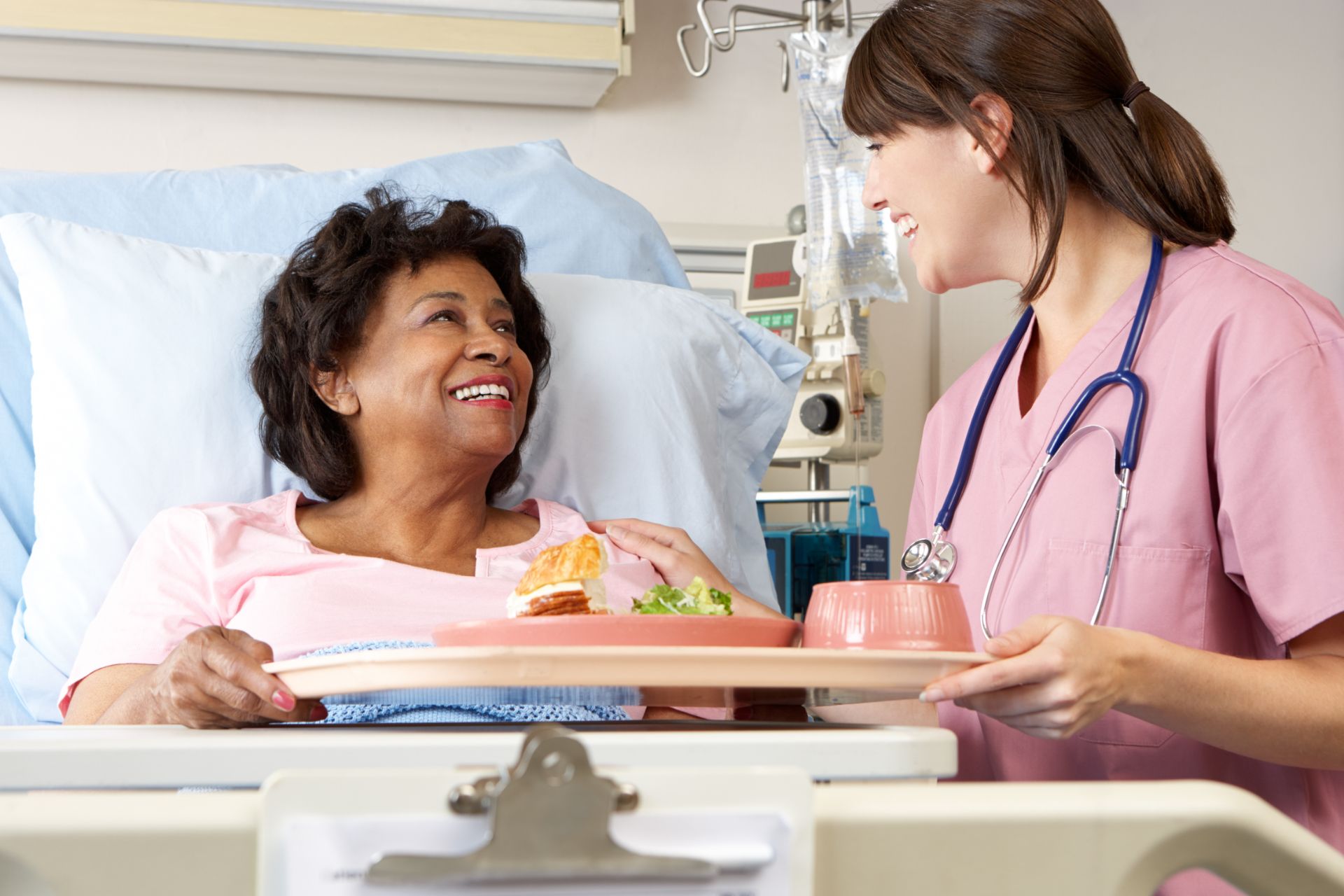 nurse serving senior female patient meal in hospital bed